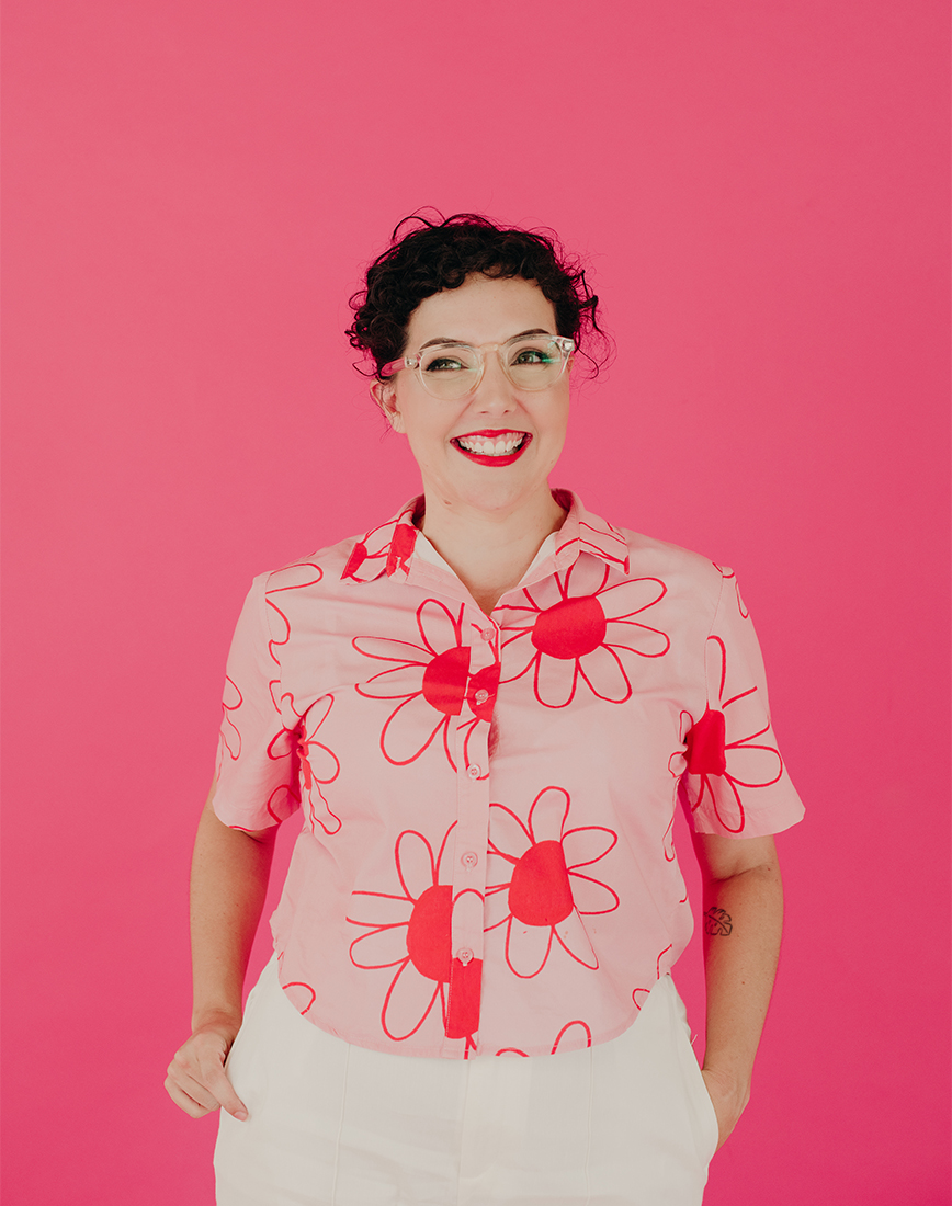 A woman smiling in front of a bright pink background.